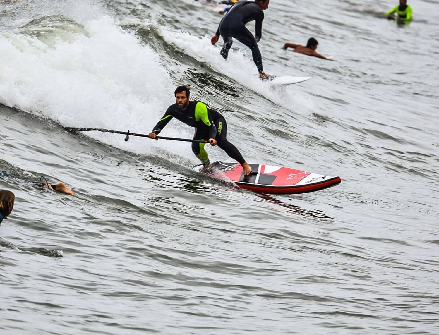 Surfista con tabla wave SPS bajando una ola junto a otro surfista